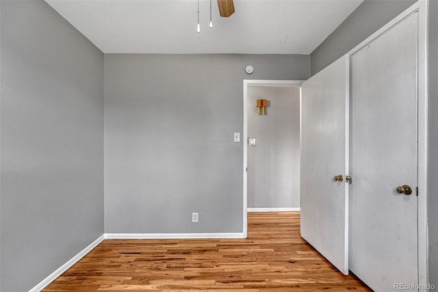 unfurnished bedroom with a closet, baseboards, a ceiling fan, and wood finished floors