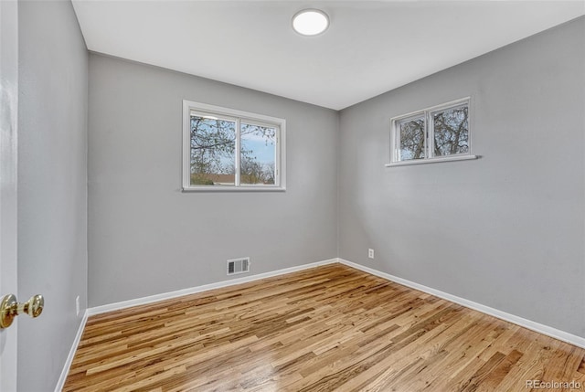 spare room featuring a wealth of natural light, visible vents, baseboards, and wood finished floors