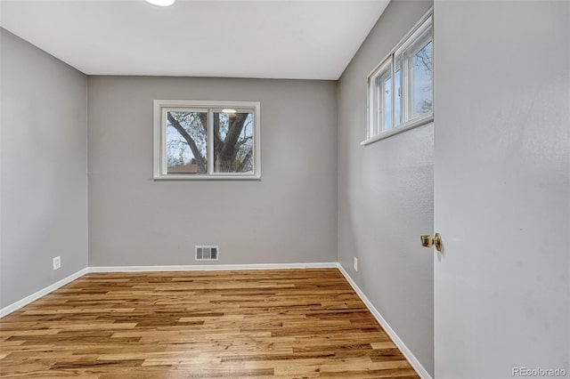 empty room featuring visible vents, a wealth of natural light, and wood finished floors