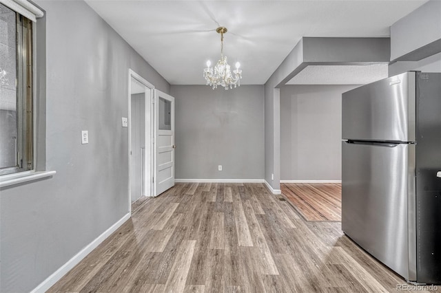 unfurnished dining area featuring baseboards, an inviting chandelier, and wood finished floors