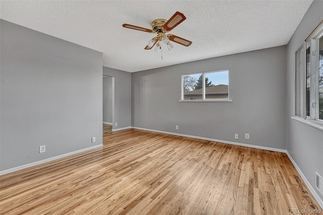 unfurnished room featuring baseboards, light wood-type flooring, a ceiling fan, and a textured ceiling