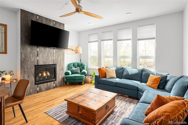 living room featuring ceiling fan, a tiled fireplace, and wood finished floors