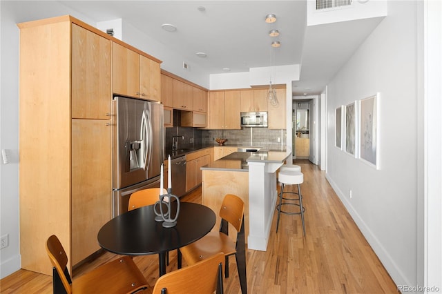 340 S Lafayette St Unit 201, Denver, CO 80209 - kitchen with appliances with stainless steel finishes, light brown cabinetry, a sink, a kitchen bar, and light wood-type flooring