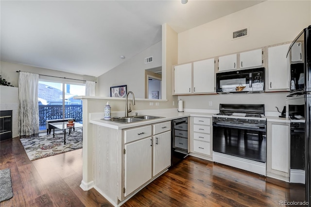 kitchen with sink, black appliances, white cabinets, a tiled fireplace, and vaulted ceiling