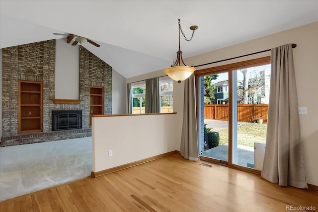 interior space featuring light hardwood / wood-style flooring, a brick fireplace, vaulted ceiling with beams, ceiling fan, and built in shelves