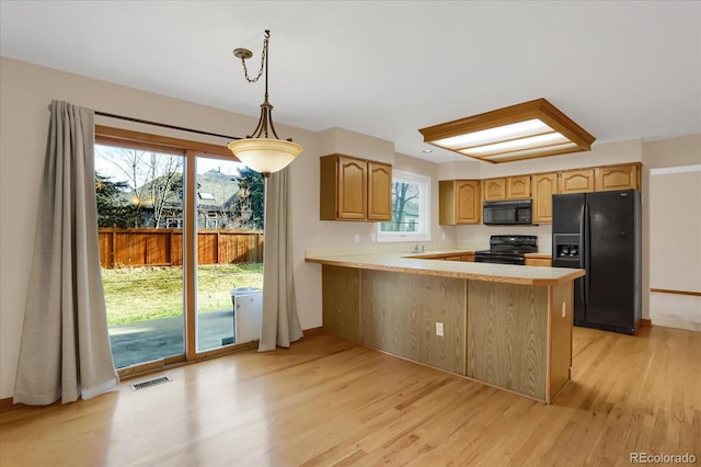 kitchen featuring black appliances, hanging light fixtures, light wood-type flooring, a wealth of natural light, and kitchen peninsula