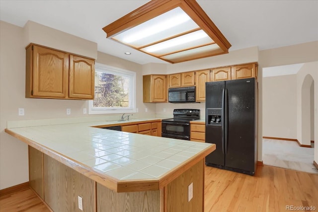 kitchen featuring sink, kitchen peninsula, tile countertops, black appliances, and light wood-type flooring