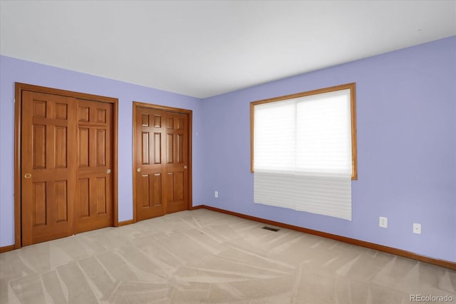 unfurnished bedroom featuring light carpet and two closets