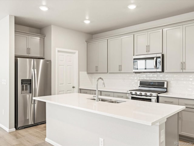 kitchen featuring stainless steel appliances, gray cabinets, sink, and a center island with sink