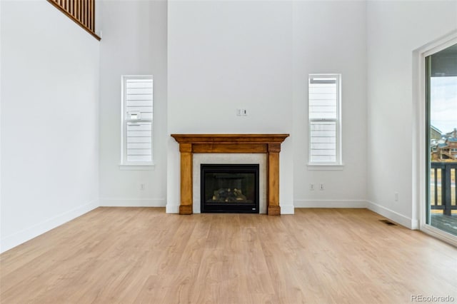 9322 Quaker St, Arvada, CO 80007 - unfurnished living room with a high ceiling, a glass covered fireplace, baseboards, visible vents, and light wood-style floors