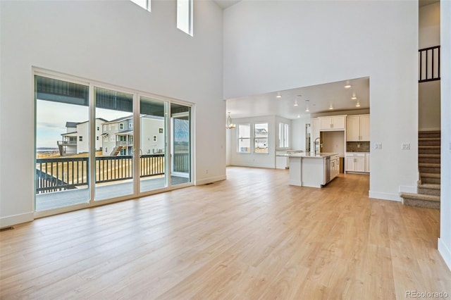 9322 Quaker St, Arvada, CO 80007 - unfurnished living room with stairs, light wood-type flooring, baseboards, a sink, and a notable chandelier