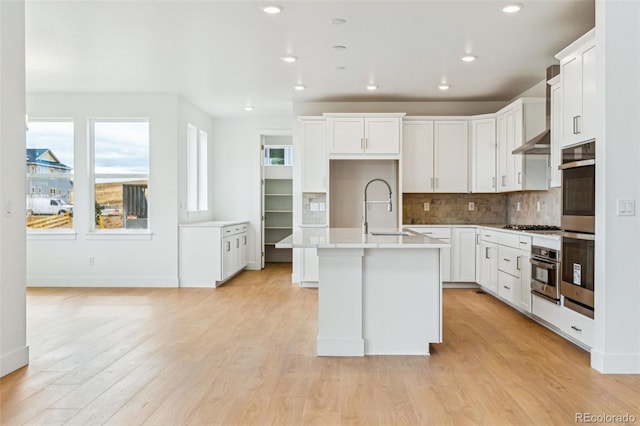 9322 Quaker St, Arvada, CO 80007 - kitchen with backsplash, a sink, light wood-style floors, a kitchen island with sink, and appliances with stainless steel finishes