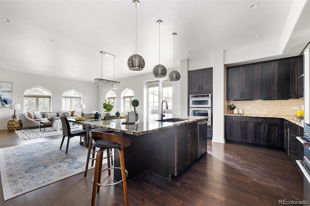 kitchen with dark hardwood / wood-style flooring, light stone counters, an island with sink, decorative backsplash, and sink