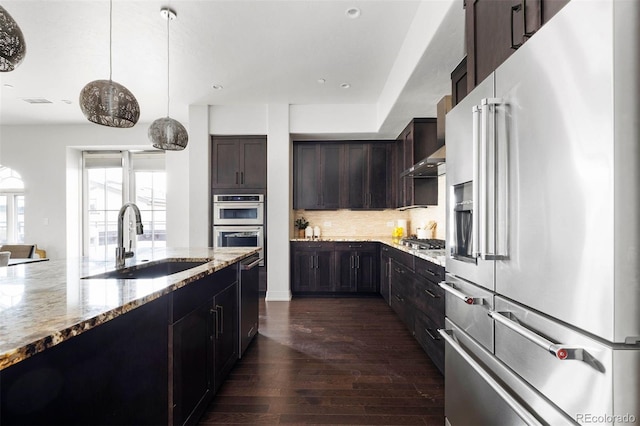 kitchen featuring decorative light fixtures, stainless steel appliances, sink, backsplash, and dark wood-type flooring