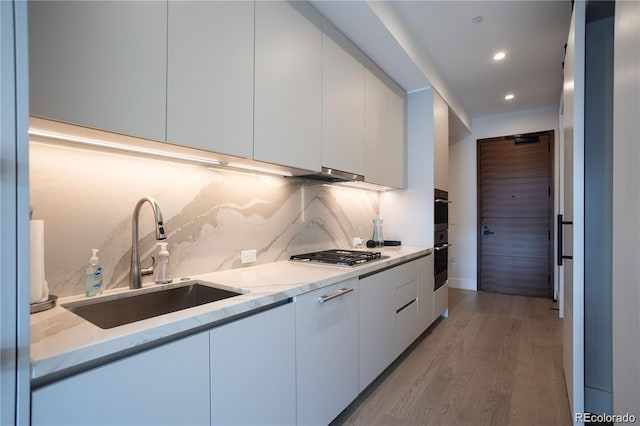 kitchen with light stone countertops, backsplash, sink, light wood-type flooring, and white cabinets