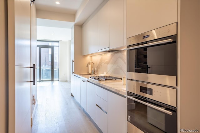 kitchen with backsplash, light hardwood / wood-style floors, sink, stainless steel appliances, and white cabinets