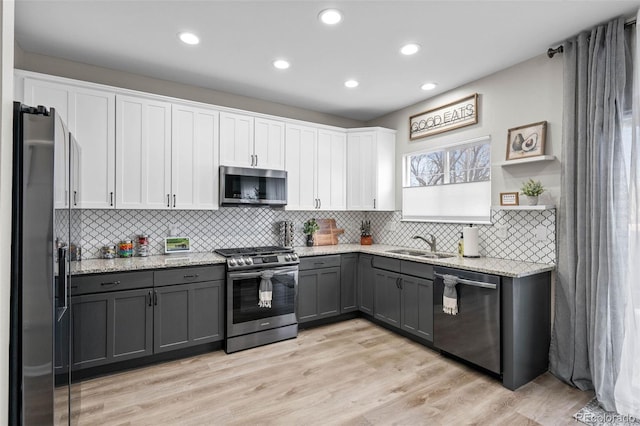 kitchen with gray cabinets, appliances with stainless steel finishes, sink, white cabinets, and light stone countertops