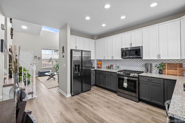 kitchen featuring gray cabinetry, appliances with stainless steel finishes, white cabinets, light stone countertops, and backsplash