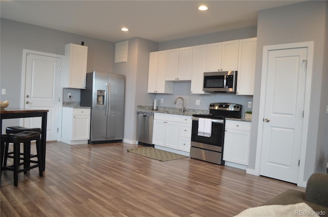 kitchen with appliances with stainless steel finishes, dark hardwood / wood-style flooring, white cabinetry, and light stone counters