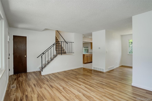 7552 Garland St, Arvada, CO 80005 - unfurnished living room with light wood-style flooring, a textured ceiling, stairway, and baseboards