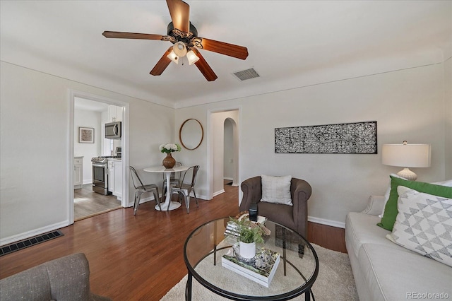 living room featuring arched walkways, wood finished floors, visible vents, and baseboards