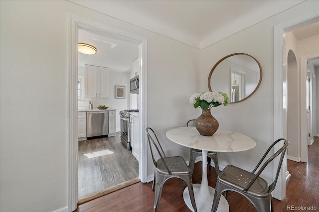 dining area with arched walkways, baseboards, and wood finished floors