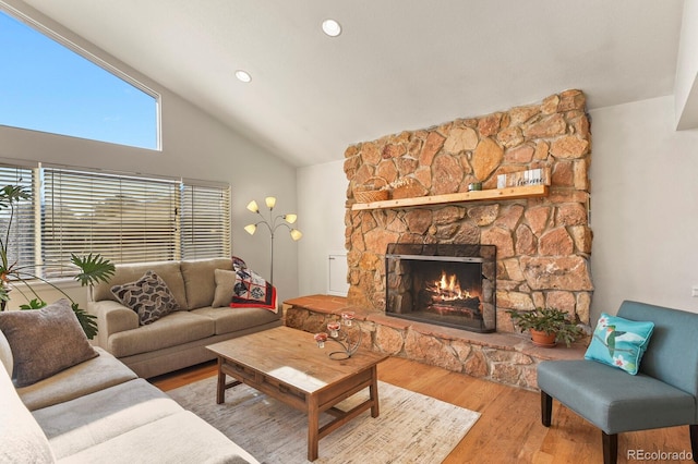 living room with high vaulted ceiling, a stone fireplace, and wood-type flooring