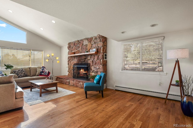 living room featuring a stone fireplace, a baseboard heating unit, a healthy amount of sunlight, and wood-type flooring