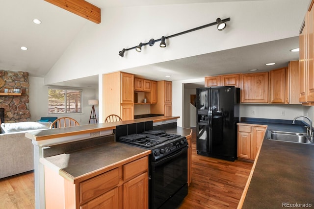 kitchen with hardwood / wood-style floors, beamed ceiling, black appliances, a fireplace, and sink