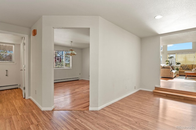 hall with a baseboard heating unit, a textured ceiling, light wood-type flooring, and a wealth of natural light