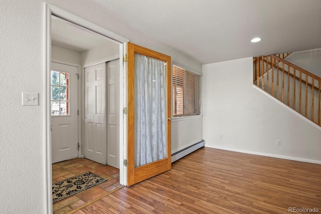 foyer entrance featuring baseboard heating, hardwood / wood-style floors, and a textured ceiling