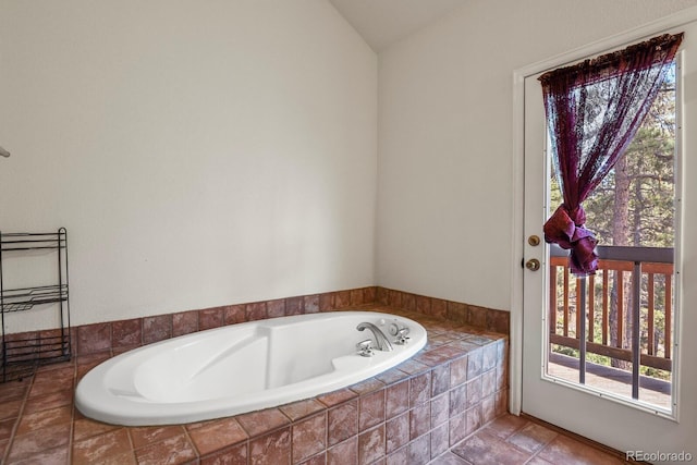 bathroom with a wealth of natural light, vaulted ceiling, and a relaxing tiled tub