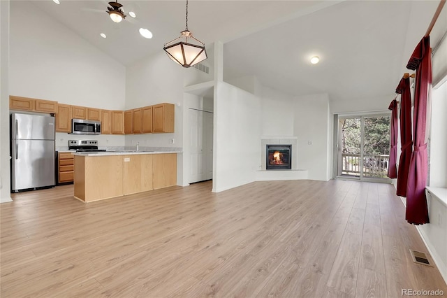 kitchen featuring stainless steel appliances, high vaulted ceiling, open floor plan, light countertops, and light wood finished floors
