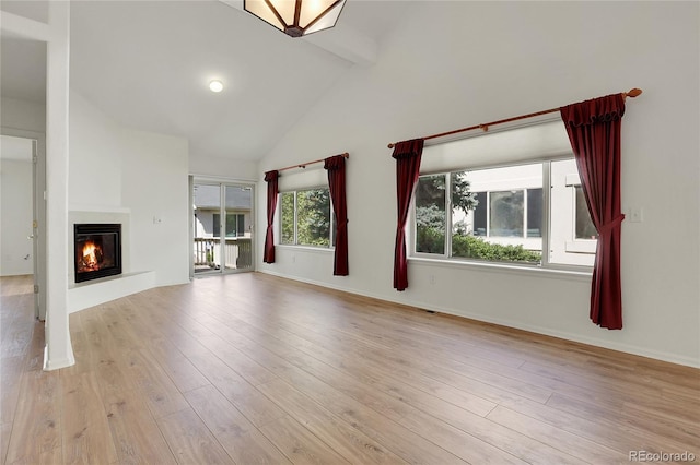 unfurnished living room featuring beam ceiling, a glass covered fireplace, wood finished floors, baseboards, and high vaulted ceiling