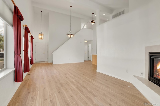 unfurnished living room featuring light wood-style flooring, a ceiling fan, a glass covered fireplace, high vaulted ceiling, and baseboards