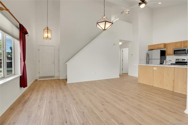 unfurnished living room featuring high vaulted ceiling, light wood-style flooring, ceiling fan, baseboards, and a sink