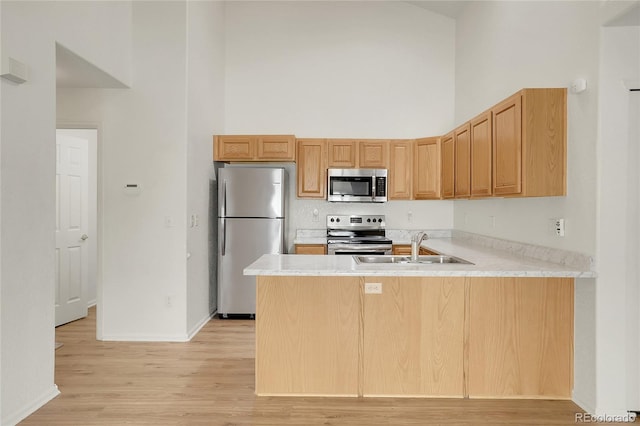 kitchen featuring stainless steel appliances, a towering ceiling, a peninsula, a sink, and light wood-style flooring