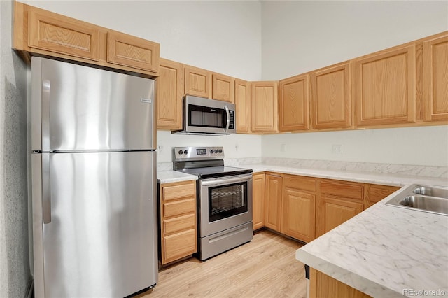 kitchen with stainless steel appliances, light wood-style floors, light brown cabinetry, light countertops, and a sink