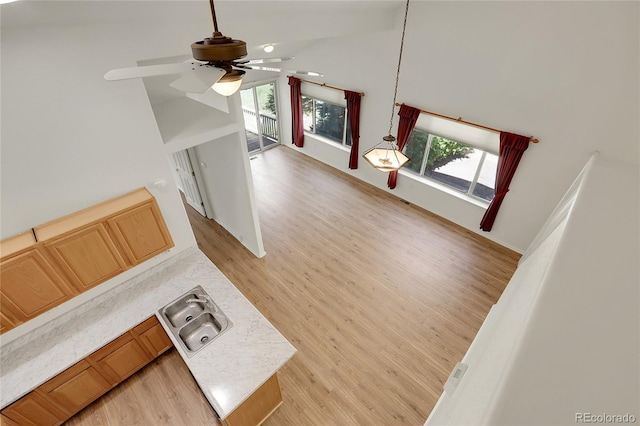 unfurnished living room with a sink, light wood-style flooring, ceiling fan, and high vaulted ceiling