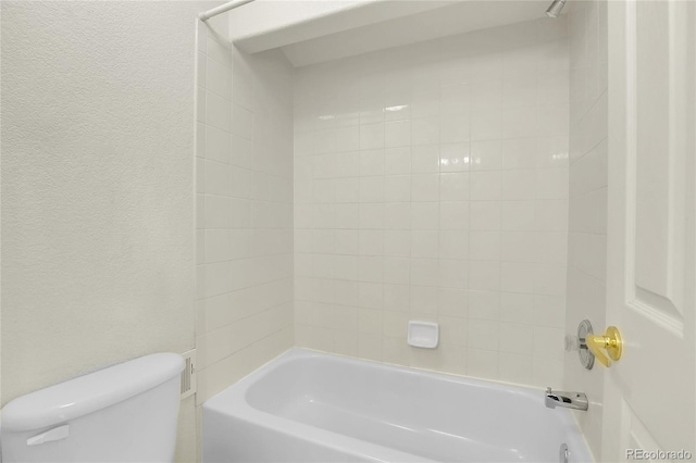 bathroom with toilet, a textured wall, and bathtub / shower combination