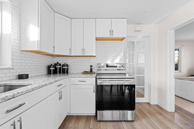 kitchen featuring electric stove, decorative backsplash, white cabinets, and light wood-type flooring