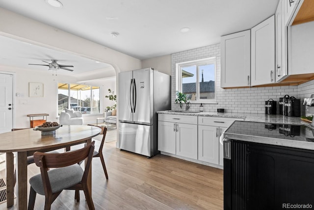 kitchen with stainless steel refrigerator, white cabinetry, light stone counters, tasteful backsplash, and light hardwood / wood-style floors