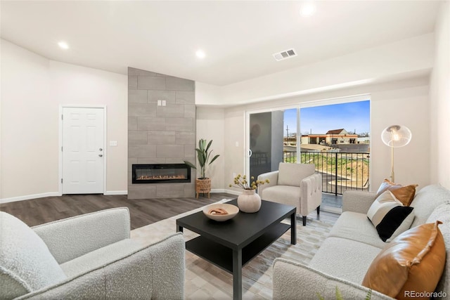 living room featuring baseboards, visible vents, wood finished floors, and a tile fireplace