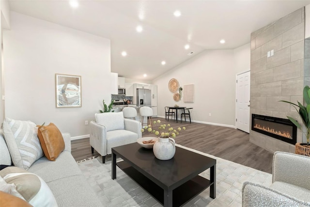 living area featuring light wood-style flooring, a tile fireplace, lofted ceiling, and baseboards