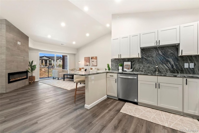 kitchen with a tile fireplace, open floor plan, dark wood-style flooring, a peninsula, and stainless steel dishwasher