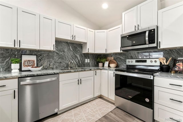 kitchen featuring lofted ceiling, appliances with stainless steel finishes, backsplash, and a sink