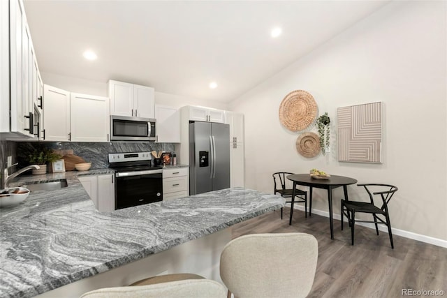 kitchen with decorative backsplash, lofted ceiling, appliances with stainless steel finishes, light stone countertops, and a sink