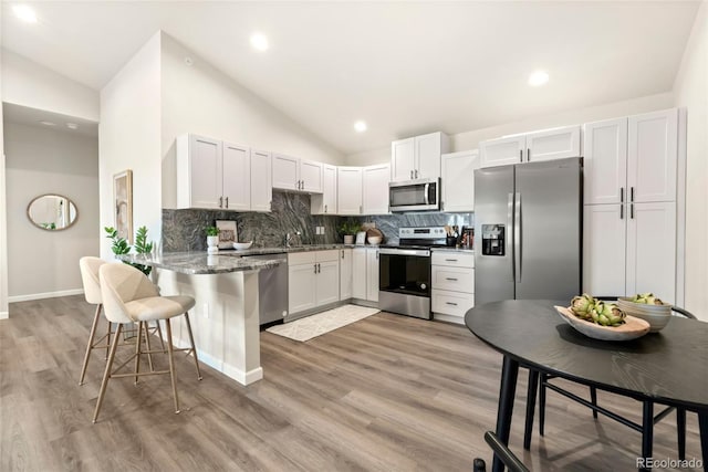 kitchen with lofted ceiling, light wood-style flooring, a peninsula, stainless steel appliances, and backsplash