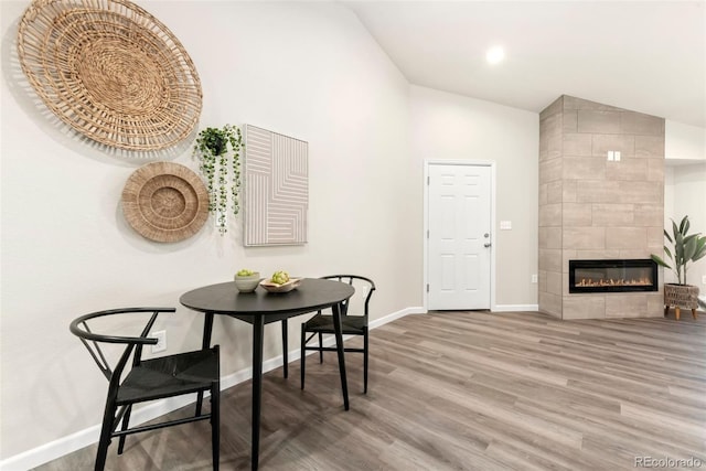 dining room featuring vaulted ceiling, a fireplace, wood finished floors, and baseboards