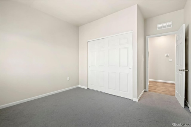 unfurnished bedroom with baseboards, visible vents, dark colored carpet, and a closet